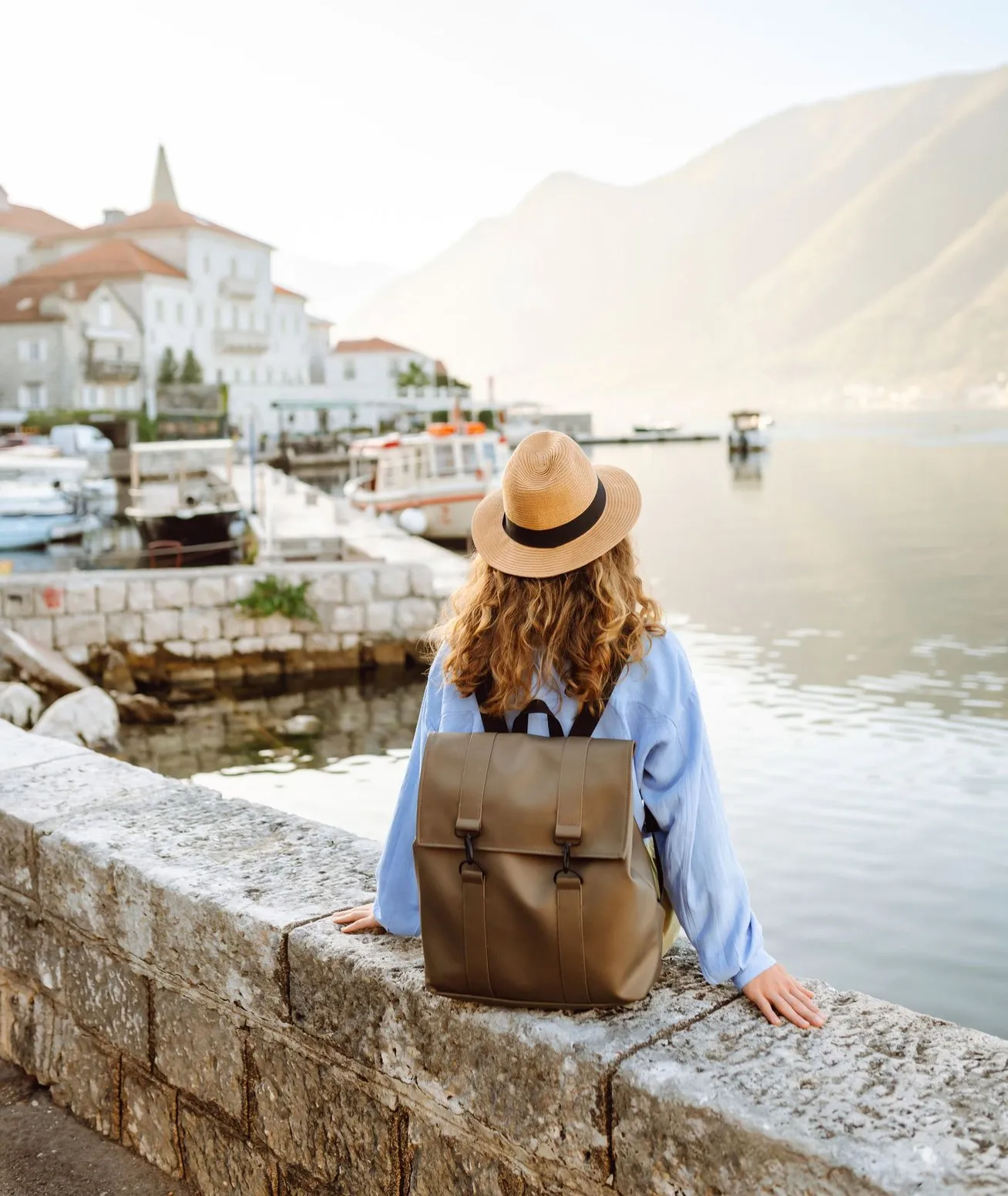 A traveller sitting on a sunny harbour wall, looking at an old town.